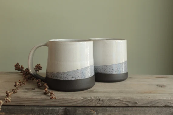 Two handmade tri-tone porcelain mugs on rustic wood with dried botanicals